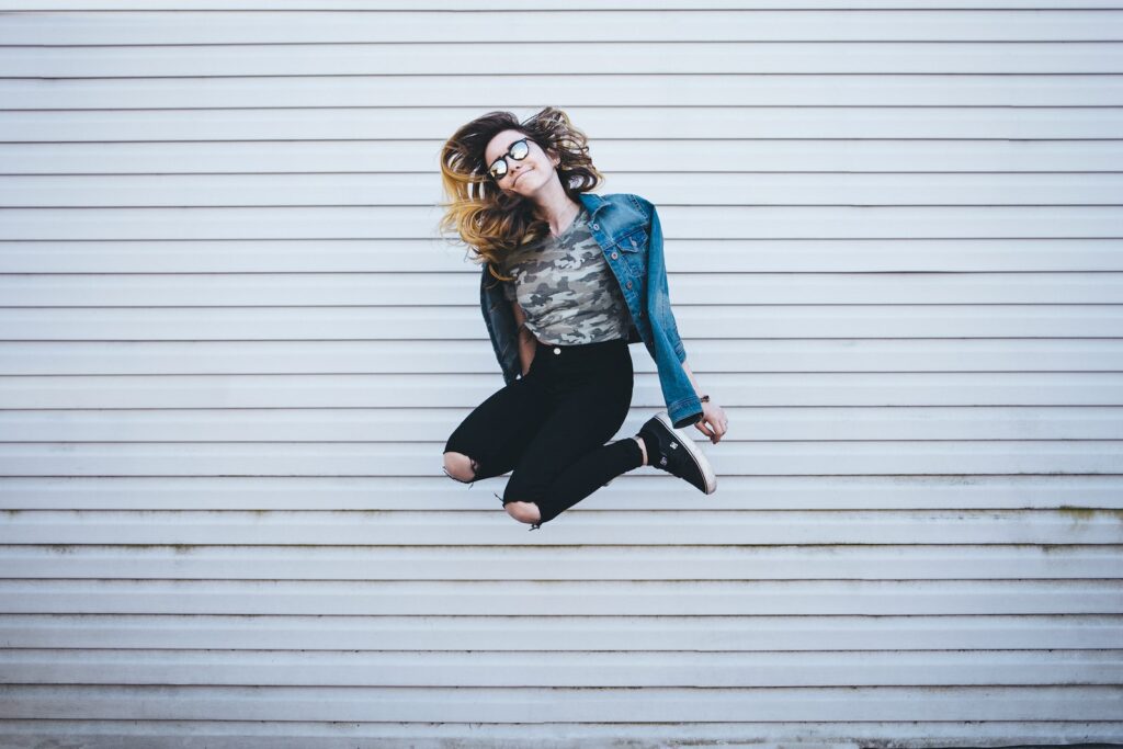 woman jumping in front of white concrete establishment - good mood