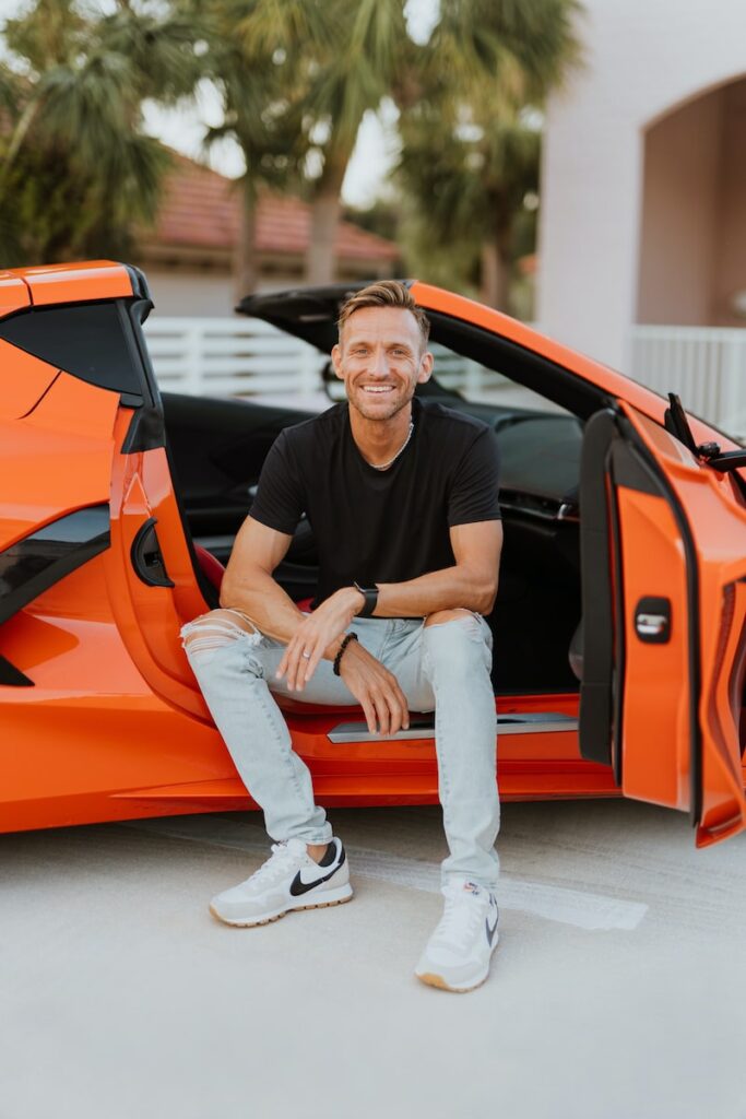 a man sitting in the open door of an orange sports car